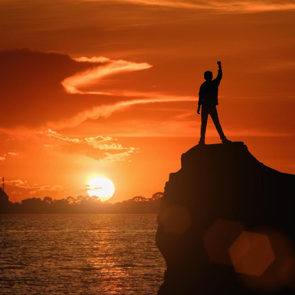 Silhouette d’un homme debout sur un sommet au coucher du soleil symbolisant le dépassement des croyances limitantes et le changement personnel